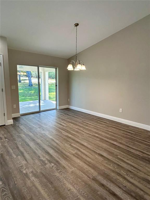 A dining area features wood-look flooring, a vaulted ceiling, a chandelier, and sliding glass doors — 15637 SE 84TH TERRACE, SUMMERFIELD, FL