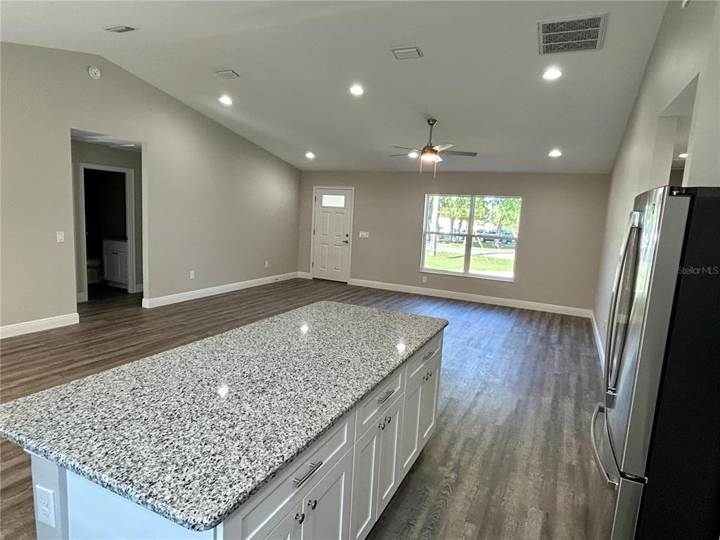A kitchen island with a granite countertop sits in an open-concept living area with flooring — 15637 SE 84TH TERRACE, SUMMERFIELD, FL