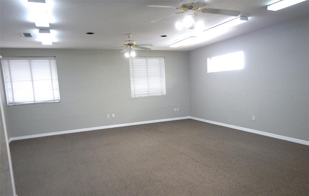 An empty room with gray walls, carpeted flooring, two ceiling fans, and multiple light fixtures — 3921 NW 97TH BOULEVARD UNIT 202, GAINESVILLE, FL