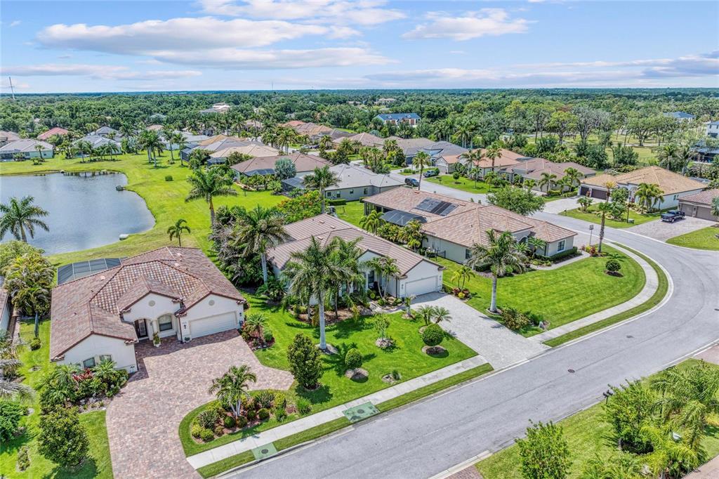An aerial view shows several suburban houses with tile roofs, palm trees, and a lake — 956 145TH STREET CIRCLE NE, BRADENTON, FL