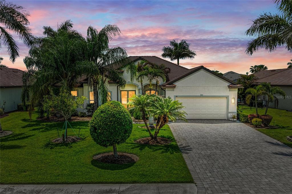 A single-story house with a paved driveway, a two-car garage, and palm trees at sunset — 956 145TH STREET CIRCLE NE, BRADENTON, FL
