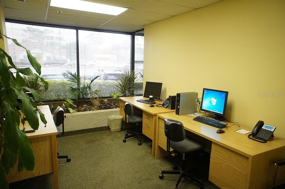 An office space features three wooden desks, computer workstations, and a large window with plants — 2101 STATE RD 434, LONGWOOD, FL