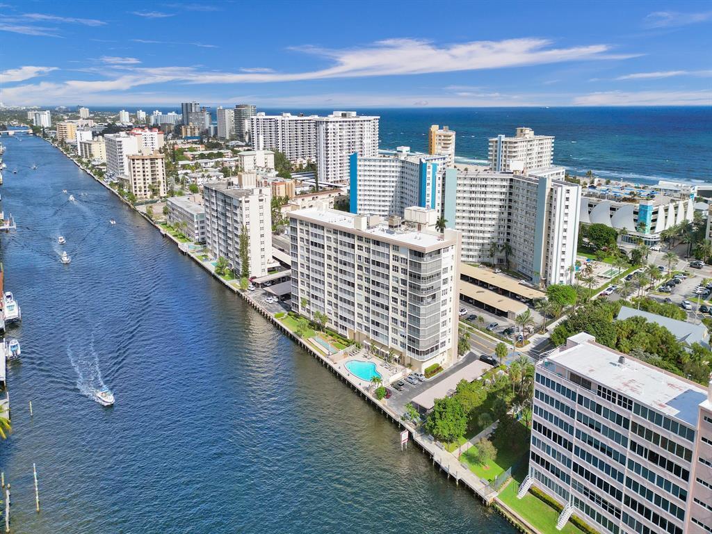 An aerial view shows a waterfront apartment building with a pool and a passing boat — 299 N Riverside Drive # 604, Pompano Beach FL 33062, POMPANO BEACH, FL