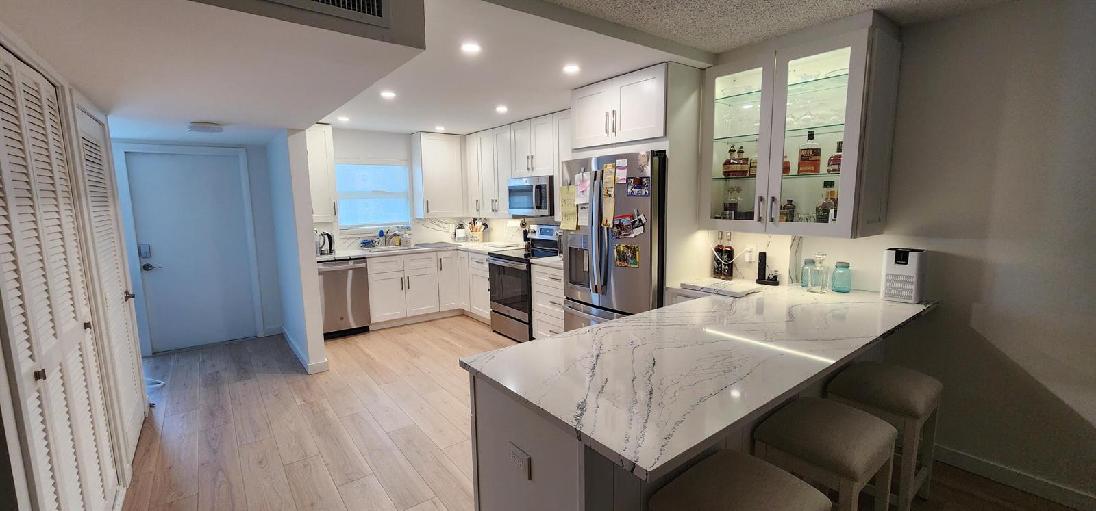A modern kitchen features white cabinetry, stainless steel appliances, and a marble-patterned breakfast bar island — 299 N Riverside Drive # 604, Pompano Beach FL 33062, POMPANO BEACH, FL