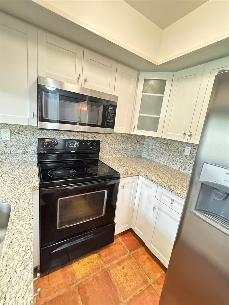 A kitchen features white cabinets, granite countertops, stainless steel appliances, and terracotta tile flooring — 8999 SW 123rd Ct # 112, Miami FL 33186, MIAMI, FL