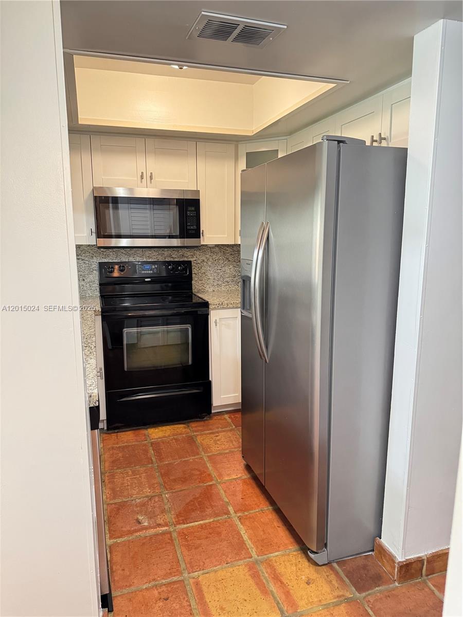 A kitchen features white cabinets, granite countertops, a black stove, and terracotta tile flooring — 8999 SW 123rd Ct # 112, Miami FL 33186, MIAMI, FL