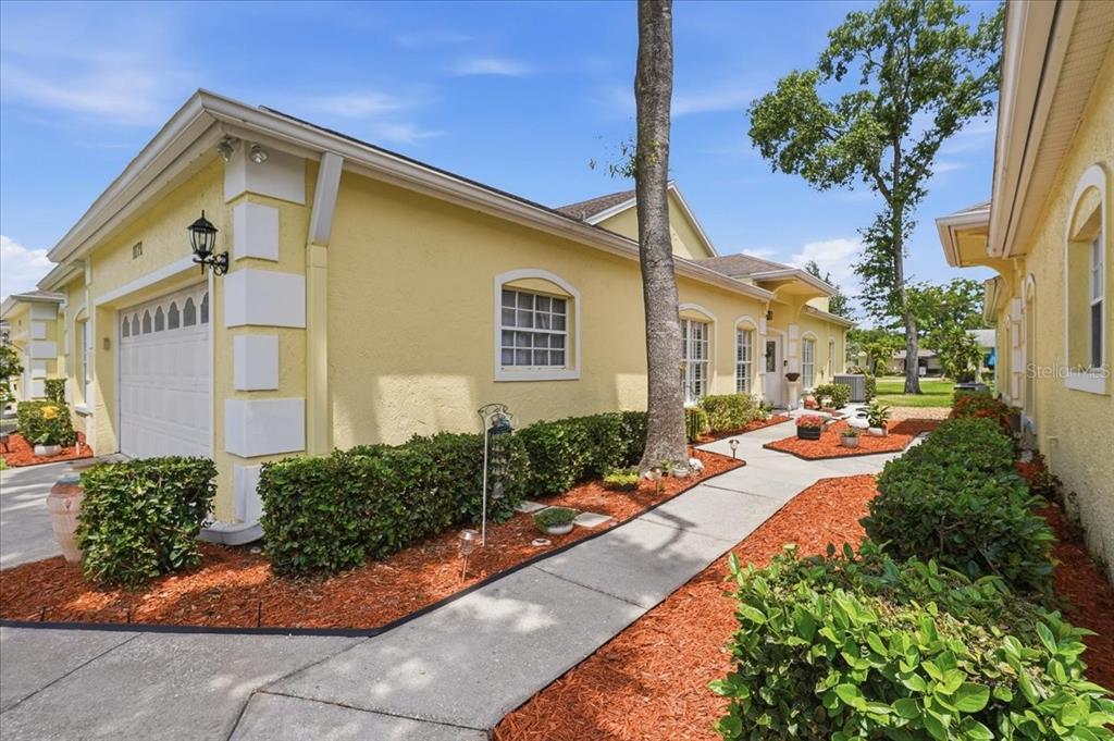 A yellow house with a white garage door and a concrete walkway through landscaped mulch — 1171 ROYAL BOULEVARD, PALM HARBOR, FL