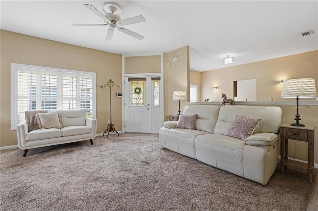 A living room features beige walls, carpeted flooring, a ceiling fan, and two white sofas — 1171 ROYAL BOULEVARD, PALM HARBOR, FL
