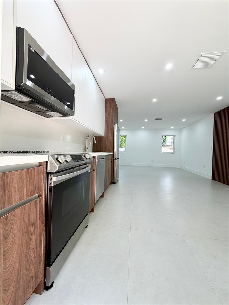 A modern kitchen features white upper cabinets, wood-grain lower cabinets, stainless steel appliances, and tile flooring — 524 NE 65th St # 2, Miami FL 33138, MIAMI, FL