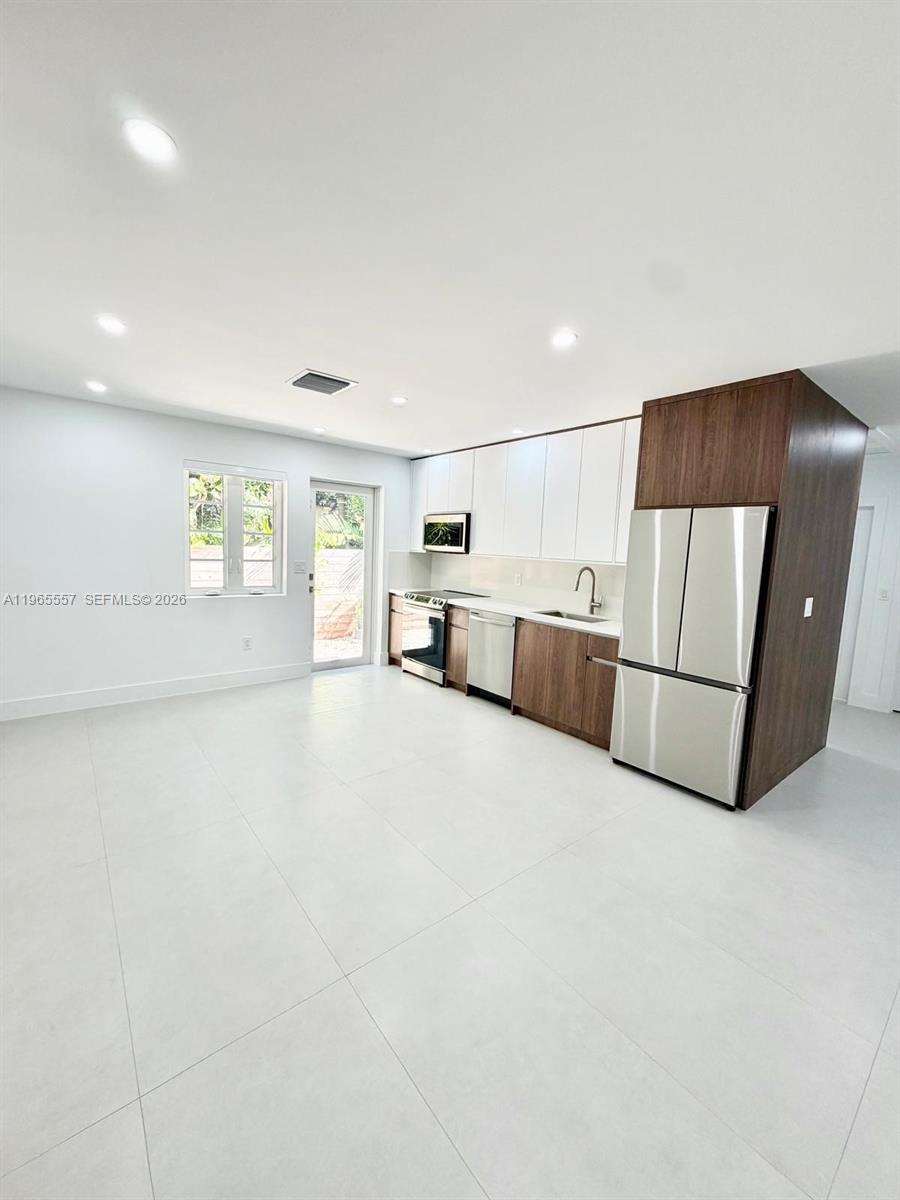 A modern kitchen features white and wood-toned cabinetry, stainless steel appliances, and light tile flooring — 524 NE 65th St # 2, Miami FL 33138, MIAMI, FL
