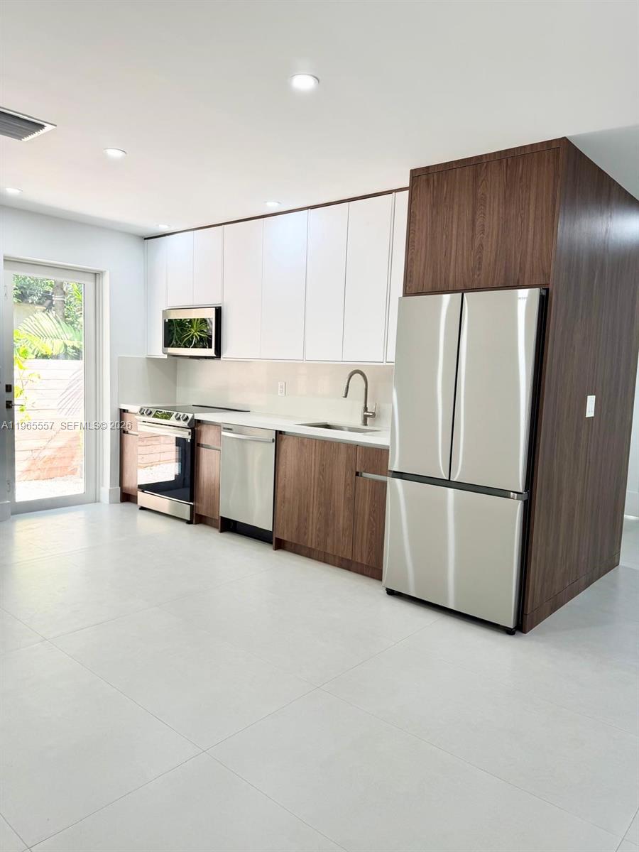 A modern kitchen features white upper cabinets, wood-tone lower cabinets, stainless steel appliances, and tile flooring — 524 NE 65th St # 2, Miami FL 33138, MIAMI, FL