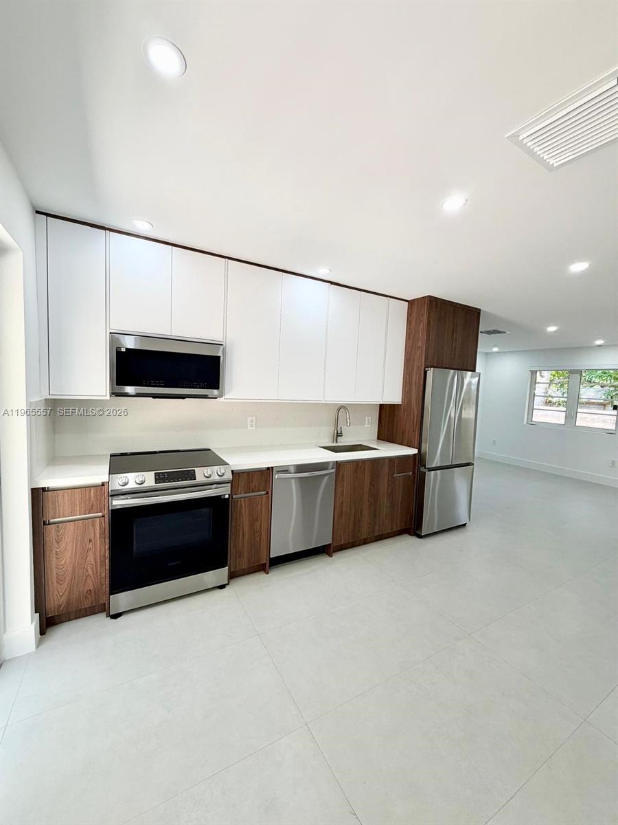 A modern kitchen features white upper cabinets, wood-grain lower cabinets, and stainless steel appliances — 524 NE 65th St # 2, Miami FL 33138, MIAMI, FL