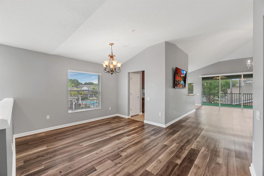 An open-concept living area features vaulted ceilings, wood-look flooring, a chandelier, and a balcony view — 2223 KINGS PALACE DRIVE UNIT 00, RIVERVIEW, FL