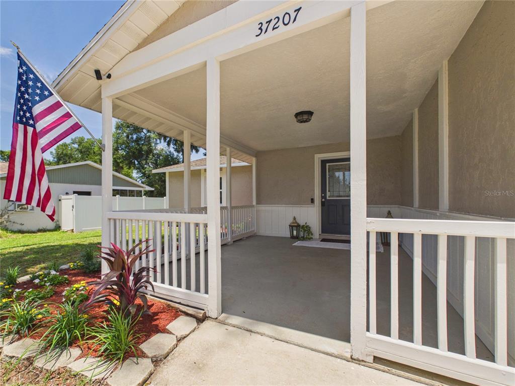 A covered front porch features a white railing, a dark blue door, and an American flag — 37207 MCMINN AVENUE, DADE CITY, FL