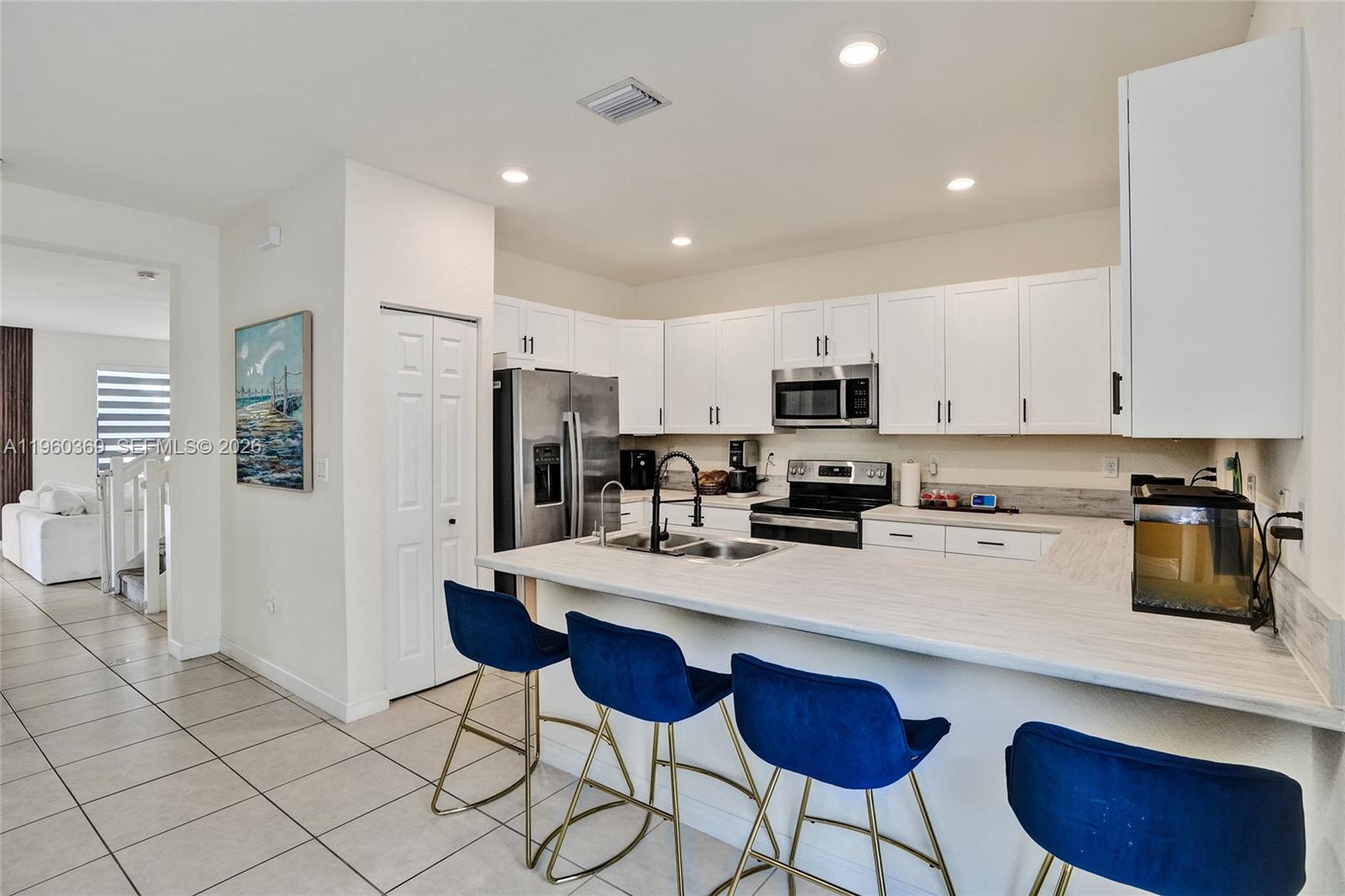A kitchen features white cabinets, stainless steel appliances, a breakfast bar, and blue bar stools — 11135 W 32nd Ln, Hialeah FL 33018, HIALEAH, FL