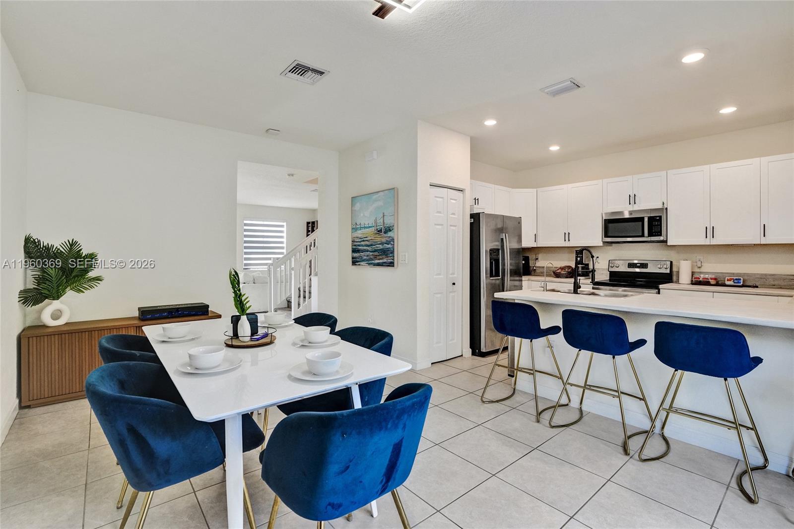 A dining area with a white table and blue chairs sits beside an open kitchen — 11135 W 32nd Ln, Hialeah FL 33018, HIALEAH, FL