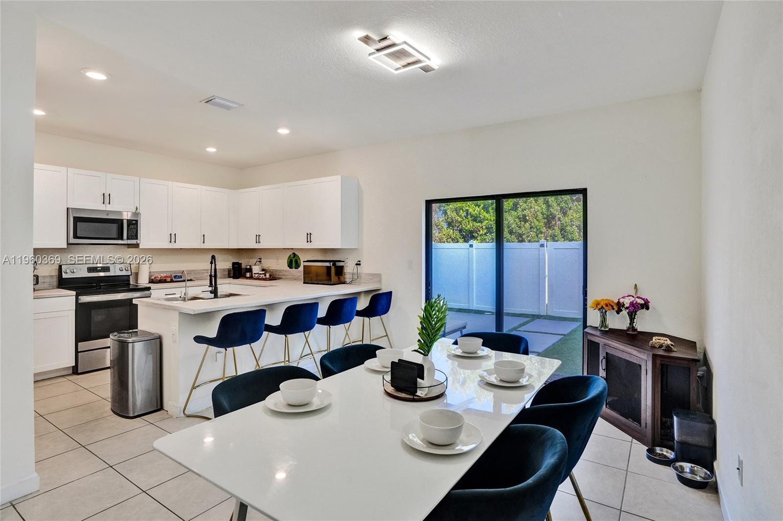 A kitchen and dining area with white cabinets, a breakfast bar, and a sliding door — 11135 W 32nd Ln, Hialeah FL 33018, HIALEAH, FL