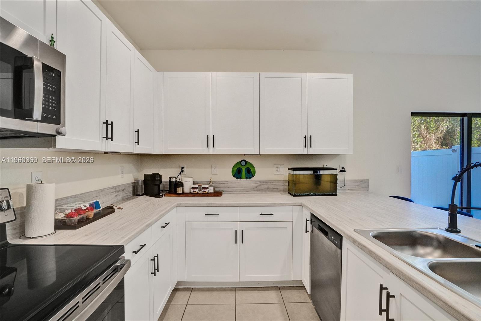 A kitchen features white cabinets, light wood-look countertops, stainless steel appliances, and tile flooring — 11135 W 32nd Ln, Hialeah FL 33018, HIALEAH, FL