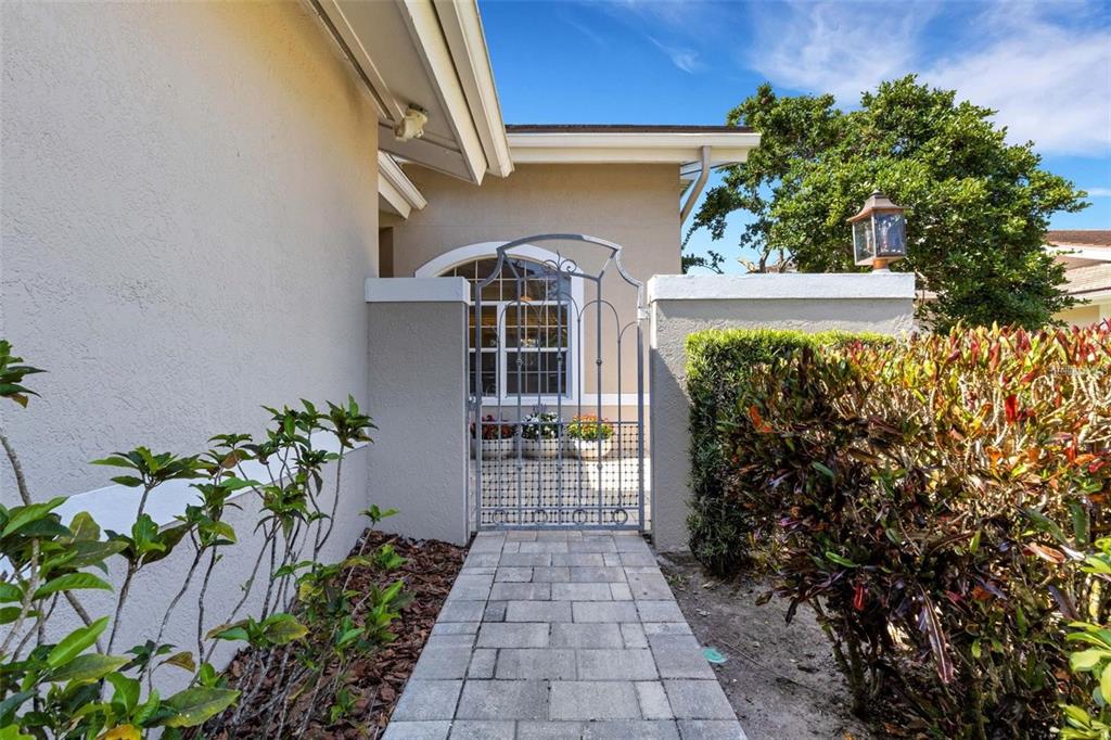 A stone walkway leads to a metal gate at the entrance of a stucco house — 4044 PENSHURST PARK, SARASOTA, FL