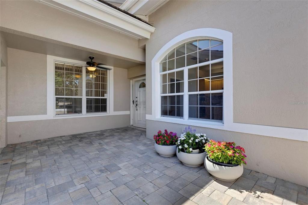 A paved patio features a white front door, a large arched window, and three potted plants — 4044 PENSHURST PARK, SARASOTA, FL