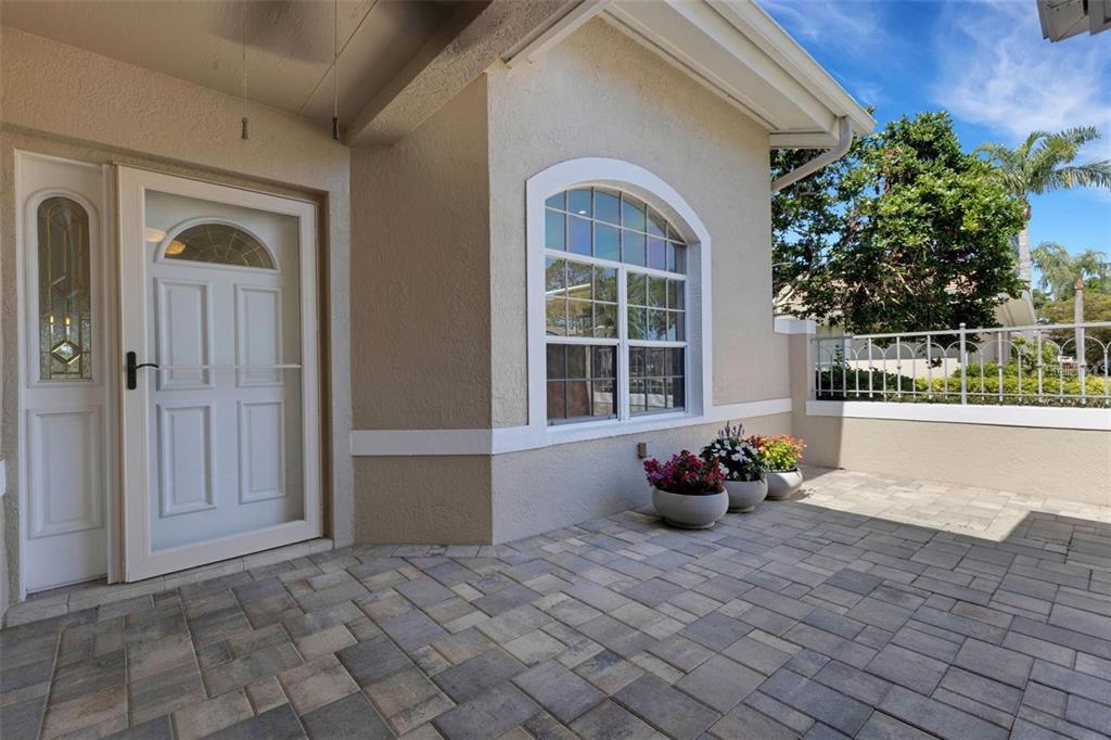 A paved entryway features a white front door, an arched window, and three potted plants — 4044 PENSHURST PARK, SARASOTA, FL