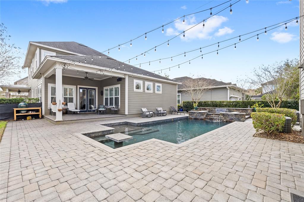 A backyard features a swimming pool, stone patio, covered porch, and overhead string lights — 14025 HENCH LANE, ORLANDO, FL