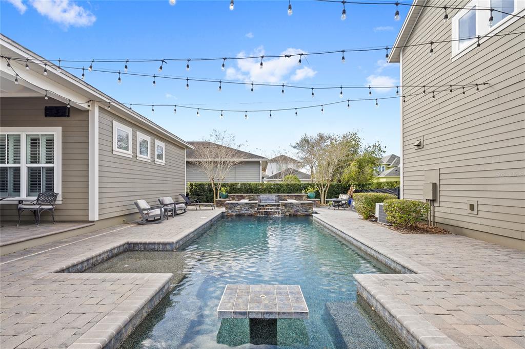 A backyard features a rectangular swimming pool with a central table and a stone waterfall — 14025 HENCH LANE, ORLANDO, FL