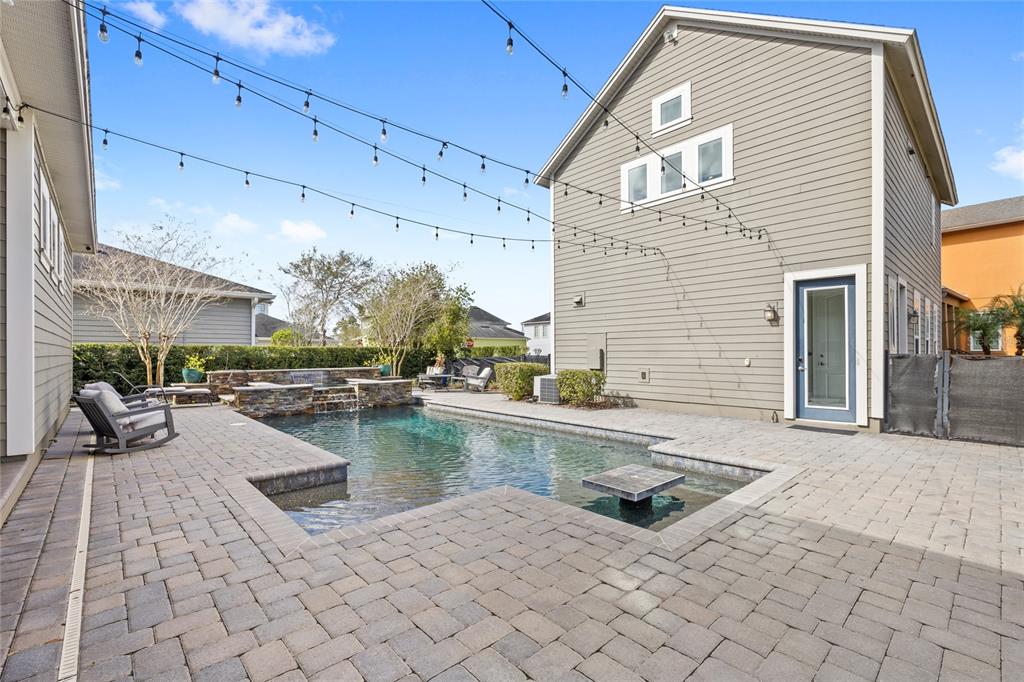 A backyard features a paved patio, a swimming pool with a fountain, and string lights — 14025 HENCH LANE, ORLANDO, FL