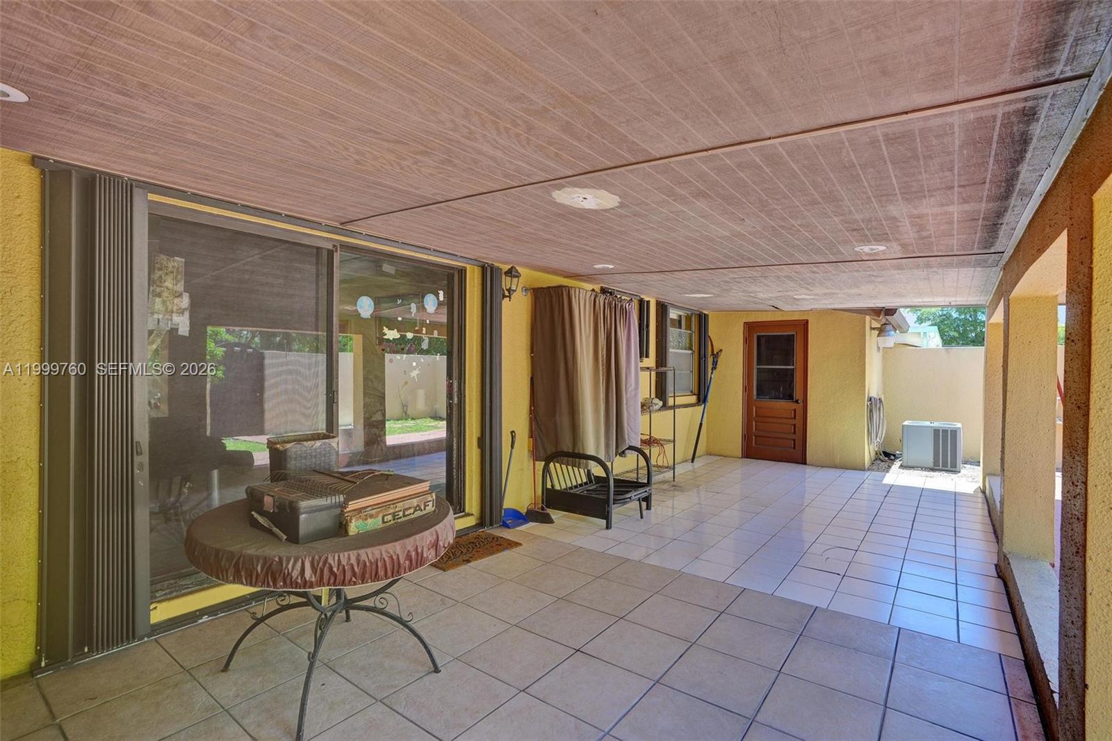 A covered patio features tiled flooring, yellow walls, a sliding glass door, and a wooden door — 8618 SW 148th Pl, Miami FL 33193, MIAMI, FL