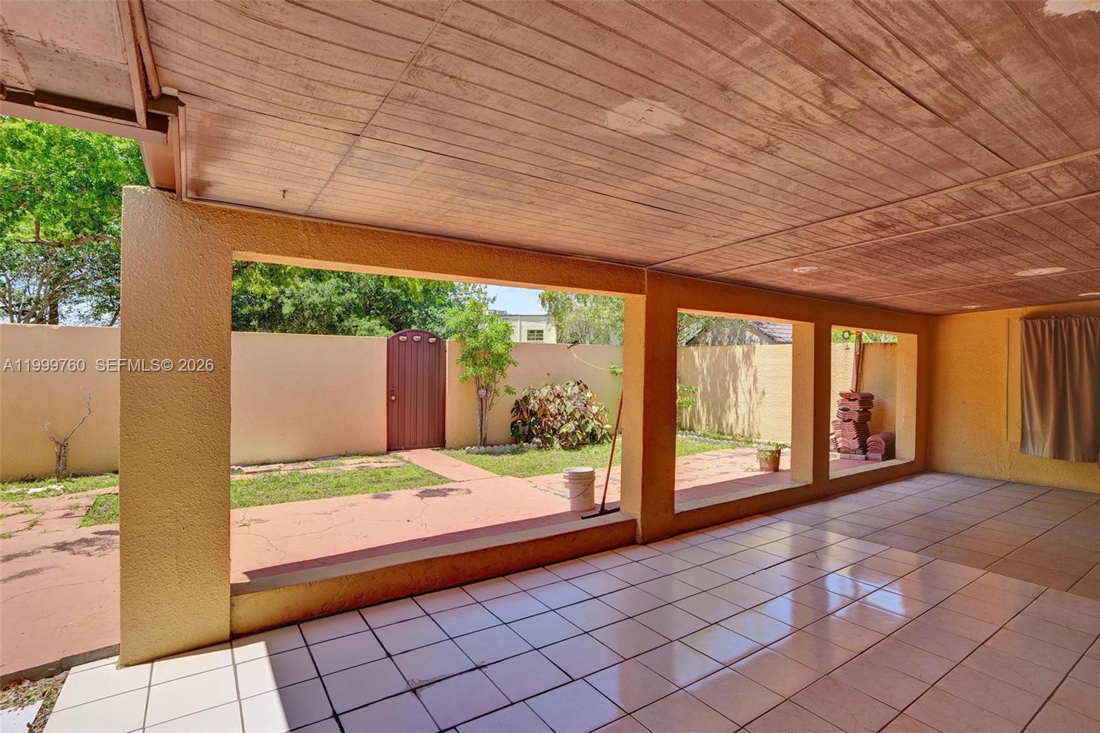 A covered patio features tiled flooring, yellow walls, and an open view of a backyard — 8618 SW 148th Pl, Miami FL 33193, MIAMI, FL