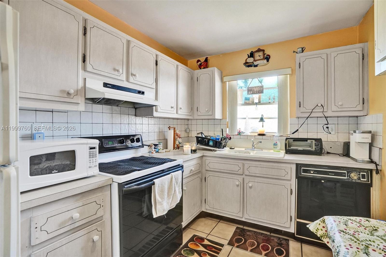 A kitchen features white cabinets, a black stove, a white microwave, and yellow walls — 8618 SW 148th Pl, Miami FL 33193, MIAMI, FL