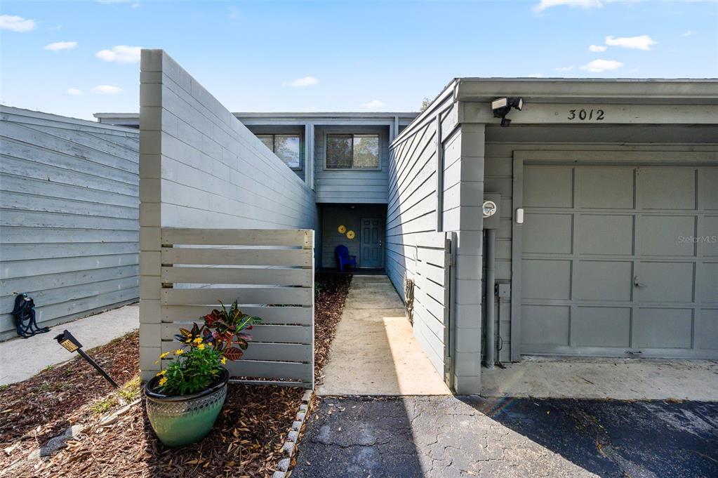 An exterior view of a gray townhouse with a garage, walkway, and privacy fence — 3012 NW 28TH CIRCLE, GAINESVILLE, FL