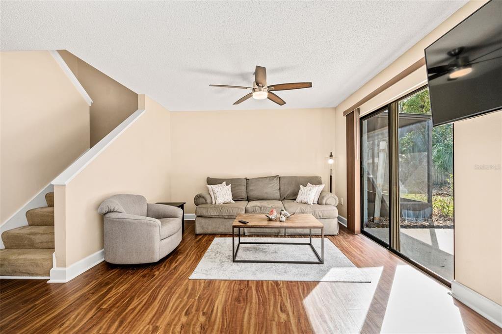 A living room features wood-look flooring, a gray sofa, an armchair, and a sliding glass door — 3012 NW 28TH CIRCLE, GAINESVILLE, FL