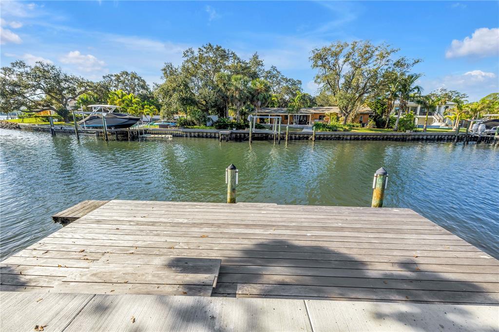A wooden dock overlooks a canal with a boat and a house in the background — 4811 PARADISE WAY S, ST PETERSBURG, FL