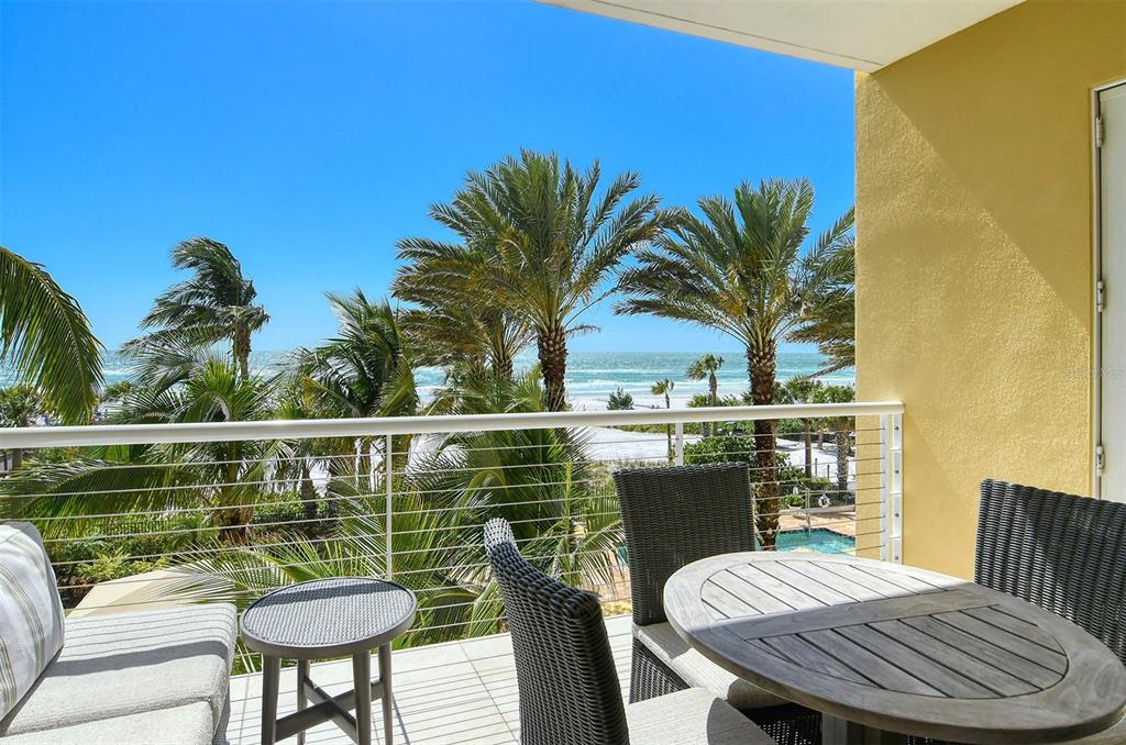 A balcony with outdoor furniture overlooks palm trees, a swimming pool, and the ocean — 915 SEASIDE DRIVE UNIT 511, Weeks 16-17, SARASOTA, FL