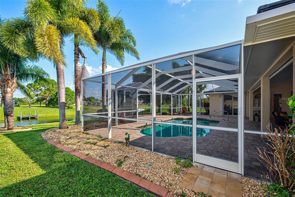 A screened-in pool patio with brick pavers overlooks a grassy yard and a small pond — 956 BOUNDARY BOULEVARD, ROTONDA WEST, FL