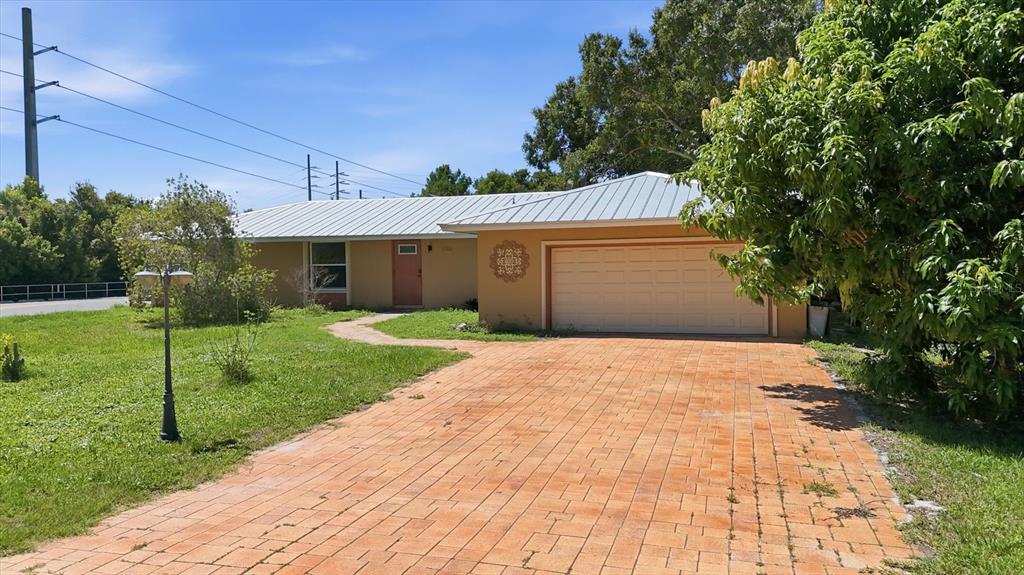 A single-story house with a metal roof, a brick driveway, and an attached garage — 1700 SPOONBILL DRIVE, NOKOMIS, FL