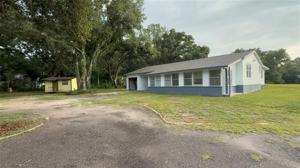 A single-story house with a gray base, white siding, and a detached shed on grass — 1051 HAWTHORN STREET, ZEPHYRHILLS, FL