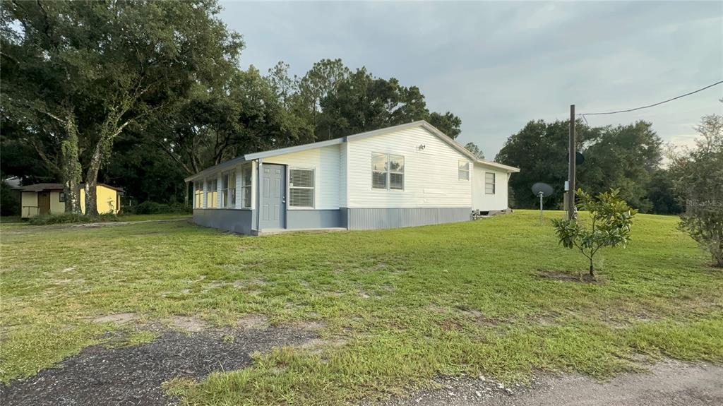 A white single-story house with a gray base and a screened-in porch sits on grass — 1051 HAWTHORN STREET, ZEPHYRHILLS, FL