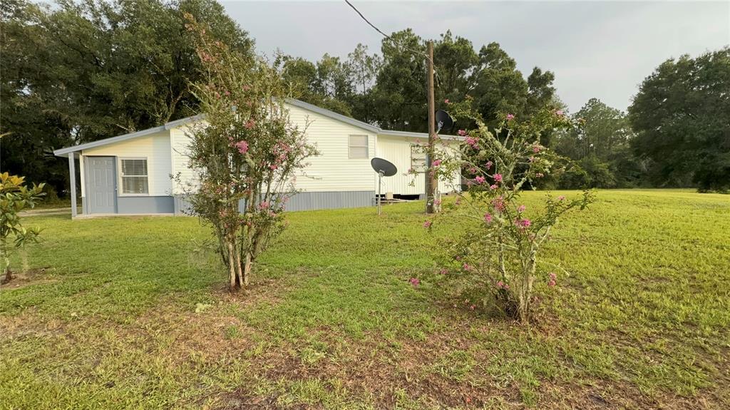 A white single-story house with a gray skirt sits on a grassy lot with trees — 1051 HAWTHORN STREET, ZEPHYRHILLS, FL
