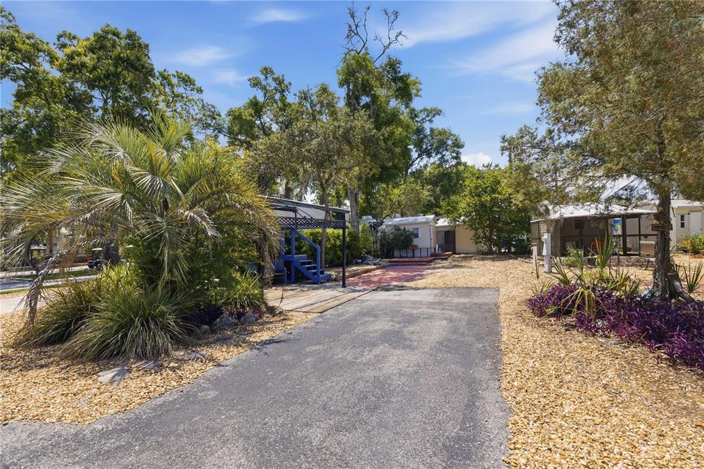 A paved driveway leads to a small house with a blue deck and gravel yard — 10173 N SUNCOAST BOULEVARD UNIT 80, CRYSTAL RIVER, FL