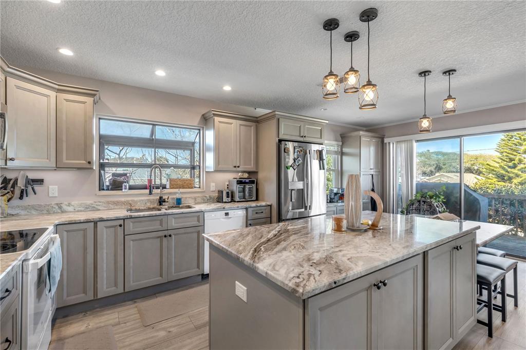 A kitchen features gray cabinetry, a large stone-topped island, and a sliding glass door — 831 E 21ST AVENUE, NEW SMYRNA BEACH, FL