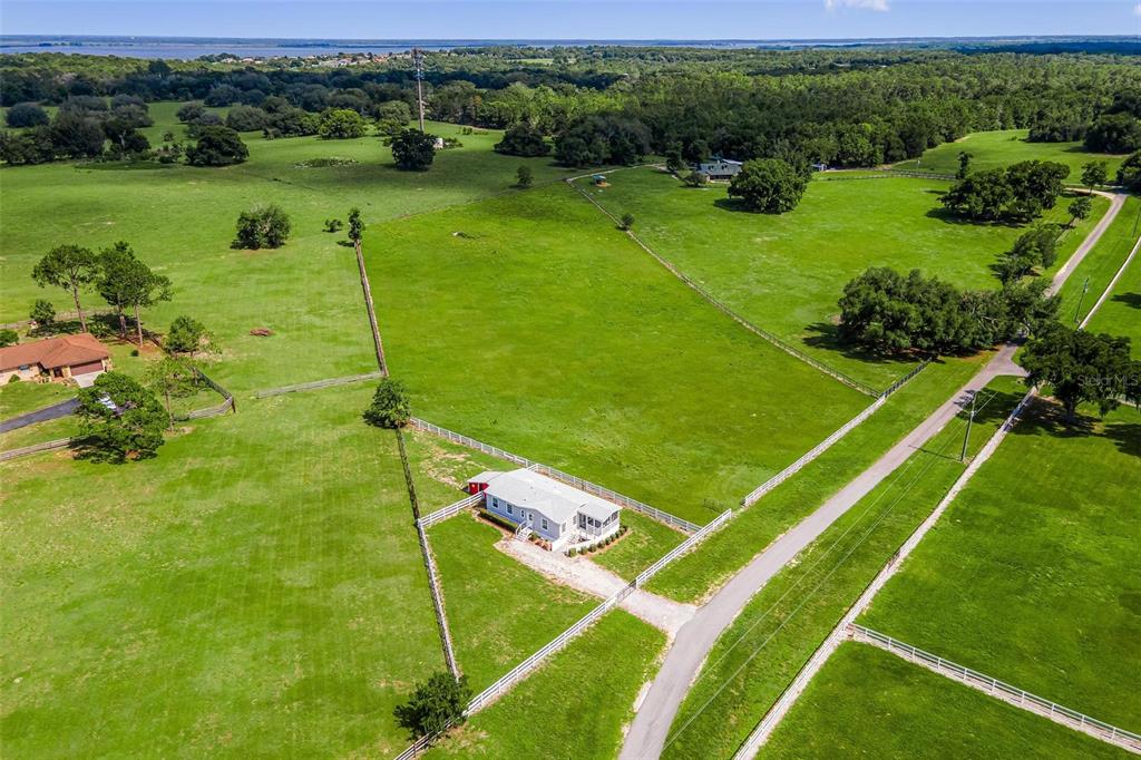 An aerial view shows a white house situated on a large, fenced green pasture — 4400 LITTLE CRITTER TRAIL, LADY LAKE, FL