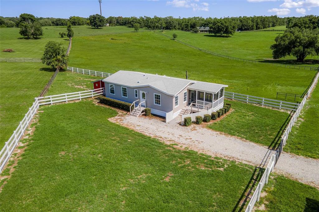 An aerial view of a light-colored manufactured home situated on a large, fenced grassy lot — 4400 LITTLE CRITTER TRAIL, LADY LAKE, FL