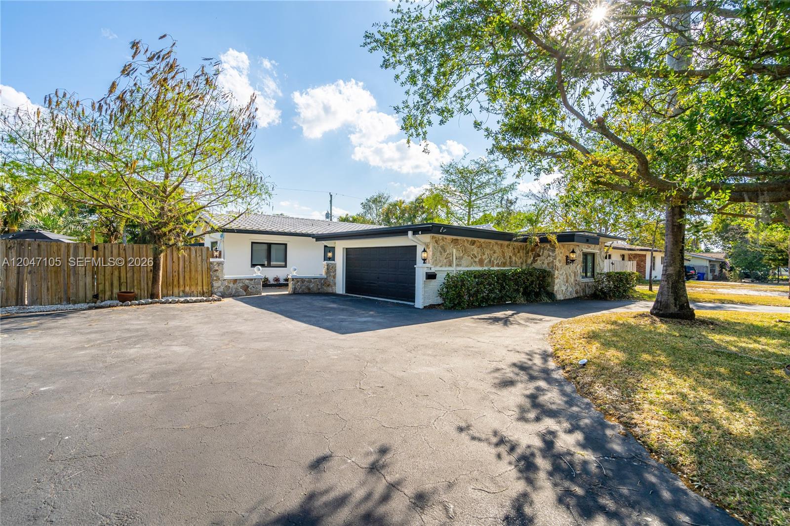 A single-story house with a stone facade, black garage door, and a large paved driveway — 714 NE 2nd St, Pompano Beach FL 33060, POMPANO BEACH, FL