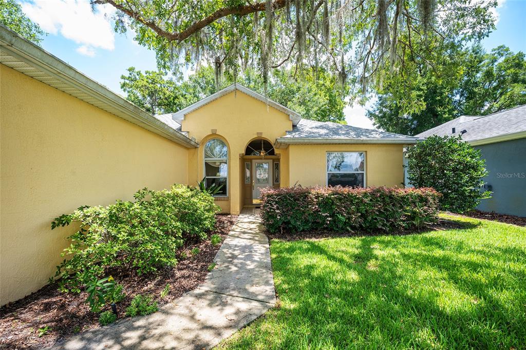 A yellow stucco house features a concrete walkway leading to an arched front entryway — 11262 SW 73RD CIRCLE, OCALA, FL