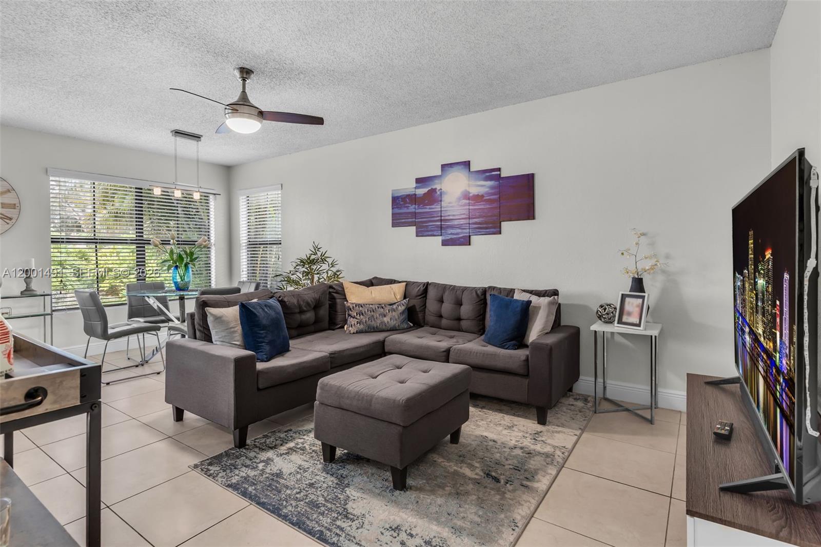 A living room features a grey sectional sofa, a matching ottoman, and a large television — 10680 SW 155th Pl # 1405, Miami FL 33196, MIAMI, FL