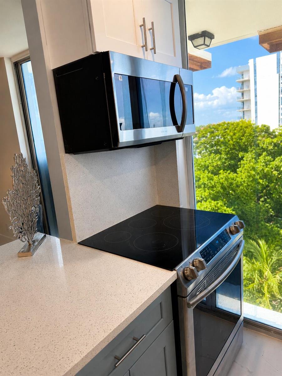A kitchen features a stainless steel microwave, electric range, and light-colored countertops beside a window — 1505 N Riverside Drive # 508, Pompano Beach FL 33062, POMPANO BEACH, FL