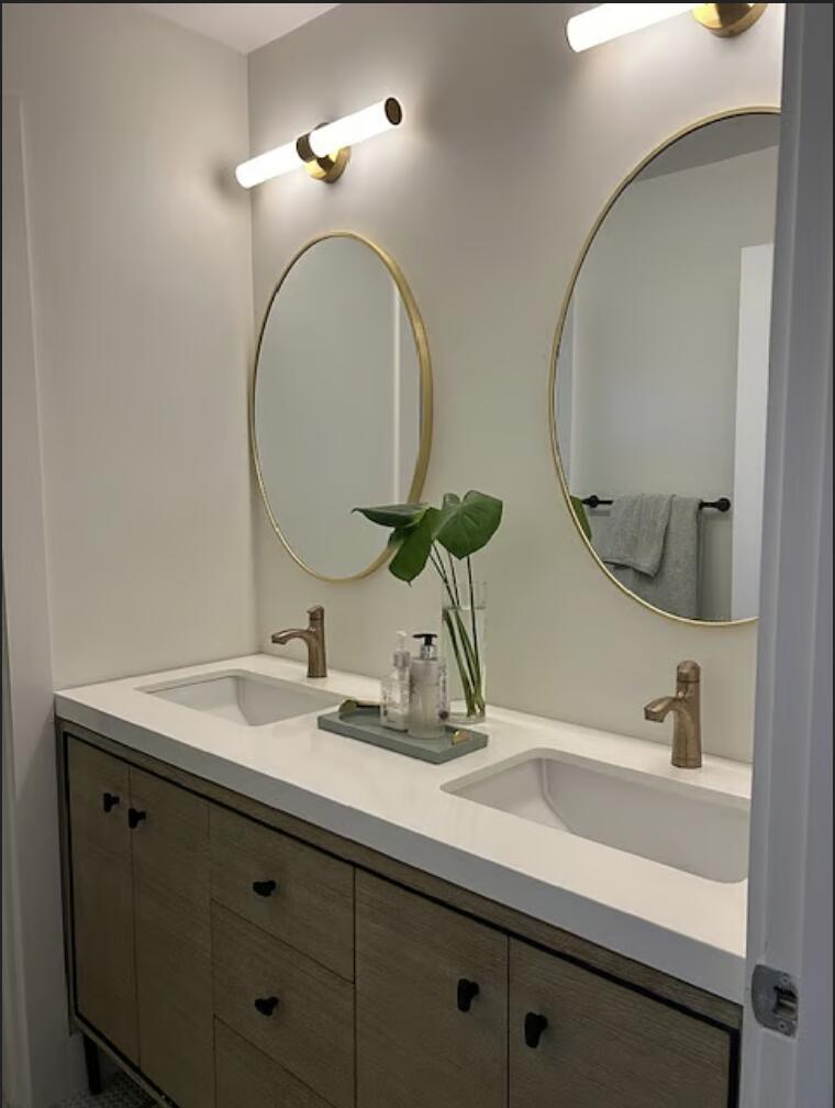 A bathroom vanity with two oval mirrors, brass faucets, and a light wood cabinet base — 1822 Windsor # 1, FL 33408, FL