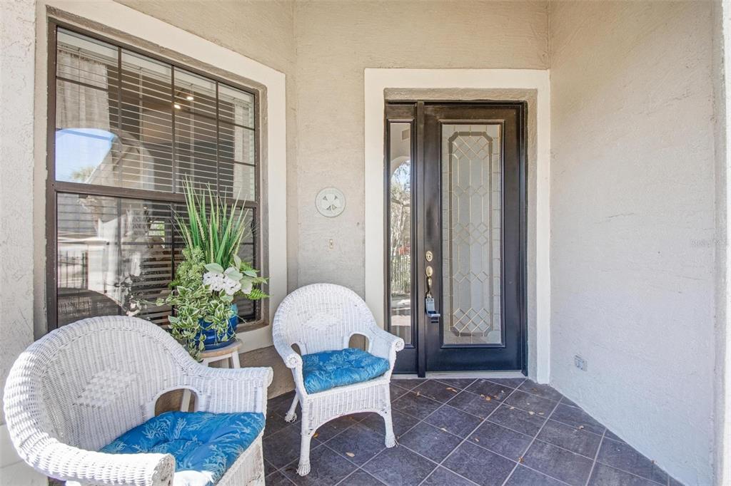 A covered front porch features two white wicker chairs, a potted plant, and a glass-paneled door — 3 RIVER PARK DRIVE N, PALM COAST, FL